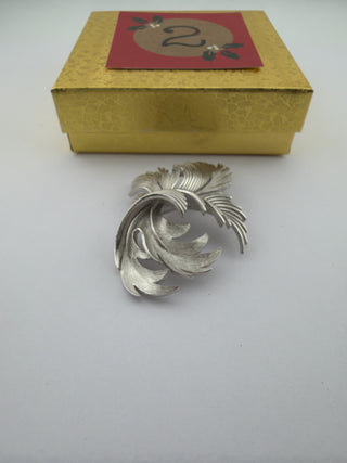 Reserved Grace vintage Trifari silver-tone leaf brooch with brushed metal texture in front of a gold gift box.
